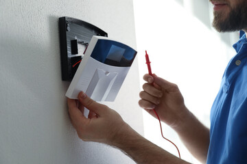 Man installing home security system on white wall in room, closeup