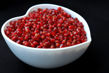 Pomegranate seeds in white heart shaped bowl, dark background