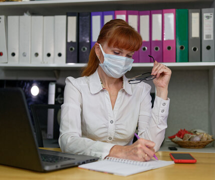 High resolution photo caucasian woman manager in a light shirt in the office in a mask working