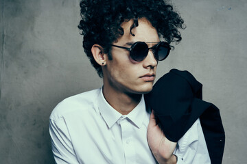portrait of a curly-haired guy in a shirt with a jacket on his shoulder and glasses on his face