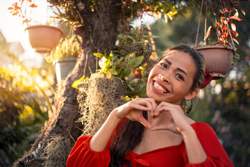 Portrait of a happy and upbeat asian transgender woman making a heart gesture while at a garden outdoors. Afternoon scene.