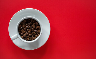 Flat lay of roasted coffee beans in white coffee on red background with copy space 