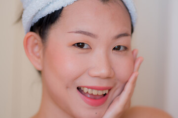  lifestyle portrait of young beautiful and happy Asian Korean woman with head towel wrap playful after applying makeup preparing for party or dating in skin care and beauty concept