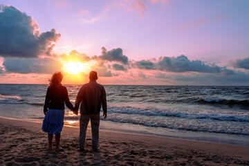 Seascape in the evening. Young couple stands on the beach in the evening and looks at the beautiful sunset