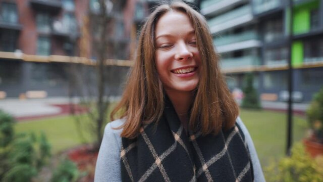 Portrait of a gorgeous dark haired woman smiling charmingly while standing against the background of modern buildings. Happy young woman enjoys life. Slow motion
