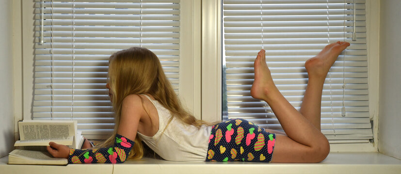 A girl with long hair is lying on the windowsill reading a book. Vacation!

