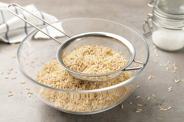 Sieve with rice in bowl on grey table
