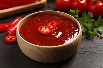 Spicy chili sauce in bowl on wooden table, closeup