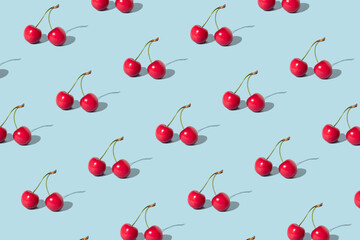 Creative pattern made with  red cherries on pastel blue background. Summer or spring fruit ...