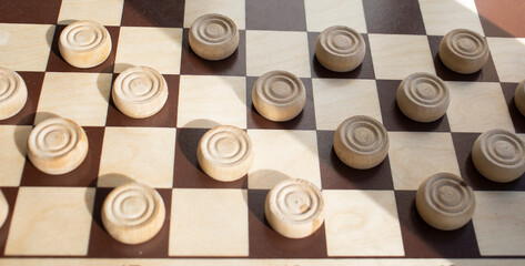 Fototapeta premium a wooden chessboard with white and brown checkers, on a light surface. Mind games, mental development and strategy. Games for children and adults. Chess school