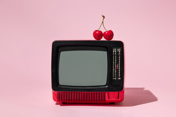 Creative layout with old tv and bright red cherry on pastel pink background. Retro style aesthetic idea. Vintage television and summer fruit concept.