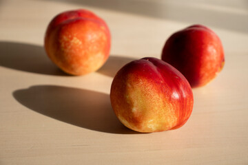 three ripe nectarines, peaches, lie on the light surface of a wooden table in the apartment. A charge of vivacity, vitamins, ripe fruits. Growing nectarine, pesticides