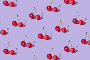 Creative pattern made with  red cherries on pastel purple background. Summer or spring fruit  concept. Minimal aesthetic idea.