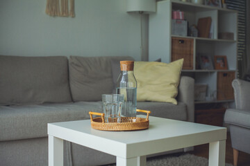 Home interior. A glass bottle with water, a glass, a rattan wicker tray on a coffee table.