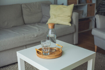 Home interior. A glass bottle with water, a glass, a rattan wicker tray on a coffee table.