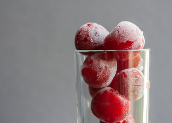 Horizontal conceptual photo of a fresh natural frozen and covered with hoarfrost sweet cherries in grass goblet on the grey background