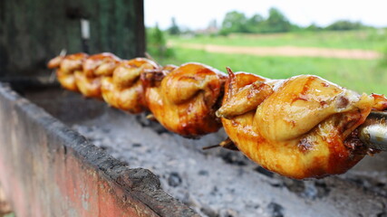 Grilled chicken swirl on the stove. Whole chicken skewers arranged on a stainless steel skewer while grilling and spinning on the charcoal grill. Selective focus