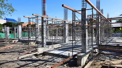 Concrete pillars with steel scaffolding of the house being built. The building structure is awaiting the curing of concrete columns for strength against a clear blue sky background. Selective focus