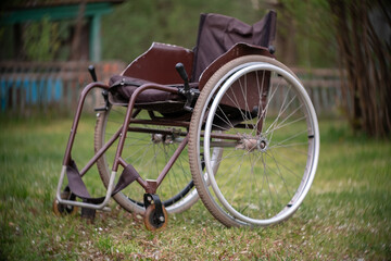 Fototapeta na wymiar Empty wheelchair standing on grass in hospital park waiting for patient services. Invalid chair for disabled people parked outdoor in nature. Handicap accessible symbol. Health care medical concept
