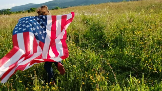 Selective focus of little playful preschool girl run across green field with national USA flag outdoors at summer day. American flag, country, patriotism, independence memorial day july fourth