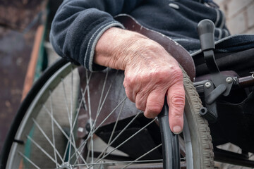 Senior disabled person hand holding pushing wheel close up view, handicapped paralyzed elderly adult grandmother invalid patient moving sitting on wheelchair, disability equipment mobility concept