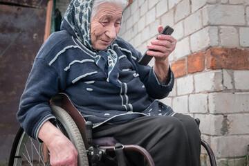 elderly woman with disabilities sitting in a wheelchair and talking on the phone. The elderly sit on the wheelchair and use the smart phone.