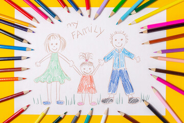 Child's drawing of a family. Mom, dad and child are drawn with pencils on a sheet of paper on a yellow background.