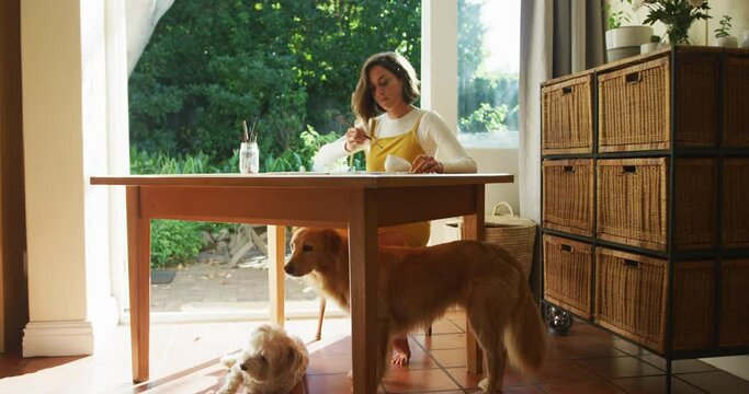 Caucasian woman painting at home with her pet dog next to her