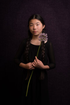 Classic studio portrait of an asian girl with a purple flower dressed in black in Rembrandt style