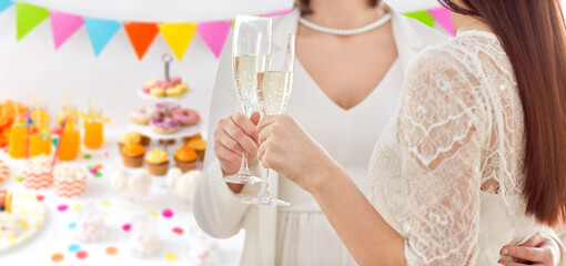 homosexuality, same-sex marriage and lgbt concept - close up of happy married lesbian couple hands holding and clinking champagne glasses over party background