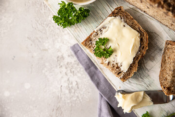 Freshly baked artisan multigrain bread with butter. Breakfast with sliced bread and butter. Light grey stone background.
