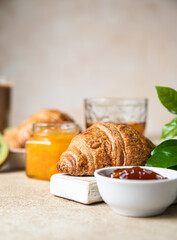 Breakfast with a cup of coffee, fresh crispy croissant, jam, kiwi and juice, light stone background. Summer breakfast.