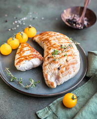 Grilled chicken or turkey breast with cherry tomatoes and thyme on a ceramic plate over green stone background.