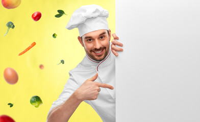 cooking, culinary and people concept - happy smiling male chef in toque with big white board over vegetables on illuminating yellow background