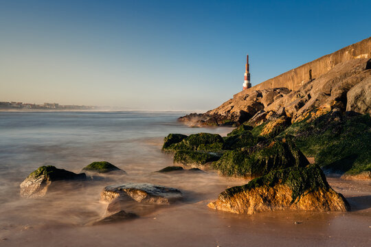 Aguda (Portugal) beach rocks and lighthouse lit by raising sun