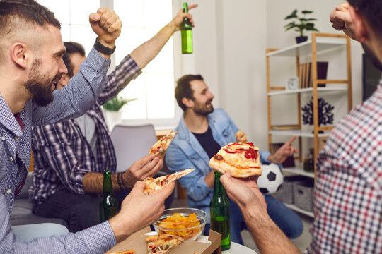 Happy young people watch a football game on TV together, eat pizza and drink alcohol. Male friendship concept, group of young friends watching sports show together.