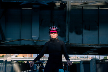 Portrait of a bicycling woman in helmet and glasses illuminated by the sun at morning trainings in the city.