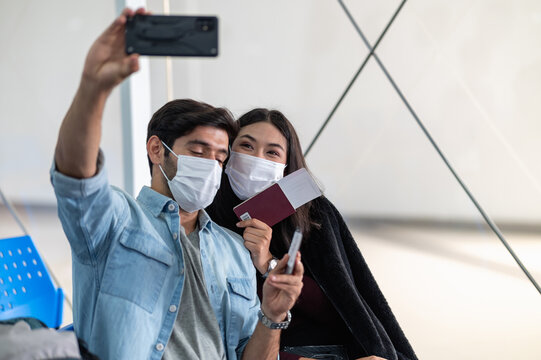 Young middle east and Asian couple wearing face mask taking selfie photo together at airport terminal before go to travel by plane prevent covid-19 infectioon follow self isolation new normal concept.