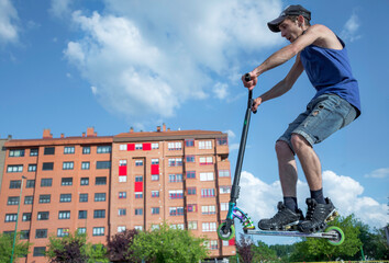 Young ride with scooter at skate park outdoors with blue sky in summer. 