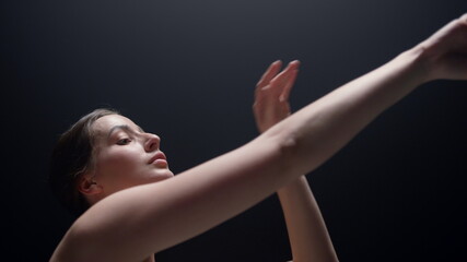 Ballet dancer practicing in dark background. Ballerina moving hands indoors.