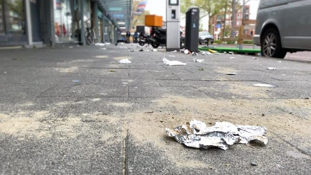 Trash on the city sidewalk near metal trash bin. Environmental protections.
