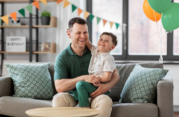 family, fatherhood and people concept - portrait of happy smiling father and little son hugging at home birthday party