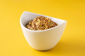 Mustard sauce in white bowl on yellow background