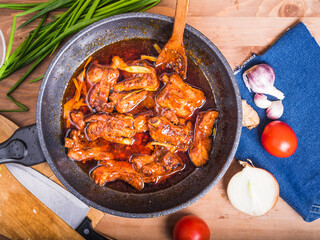 Pork ribs stewed in sweet and sour sauce in a large wok on the table with ingredients for cooking, top view. Spicy braised pork