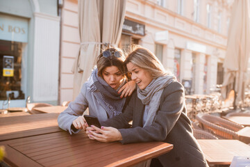 Two beautiful caucasian blondes shopping in the city. Caucasian girls sit in a cafe and look at the phone