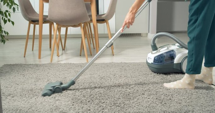 Unrecognizable woman cleaning dust and debris from carpet using a vacuum cleaner at home.