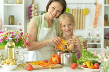 Cute little girl with her mother cooking together at kitchen table