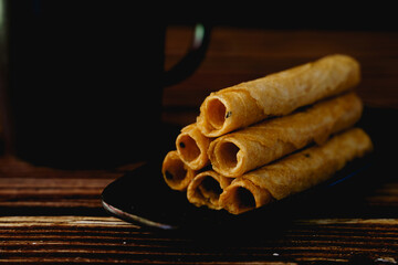 Tong Muan or Thai rolled wafer with a black cup on wooden table.