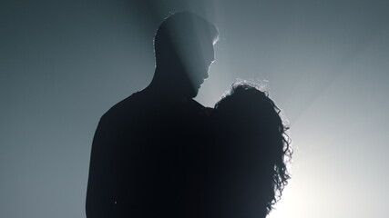 Silhouette guy and girl embracing in dark space. Romantic couple dancing.