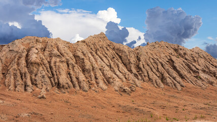 A large mound of sandy soil eroded by rainwater and sky clouds.